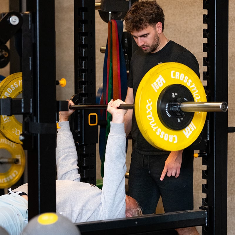 Ondernemer begeleid door sportmedisch personal trainer tijdens het bankdrukken bij WOOO Personal Coaching in Brecht, Antwerpen